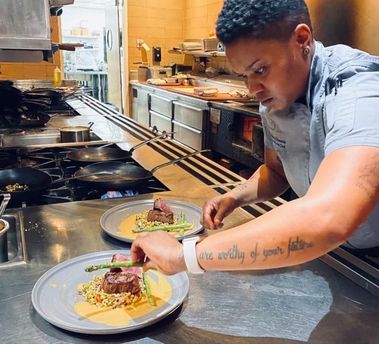 Chef Tina plating a fine-dining dish in a professional kitchen
